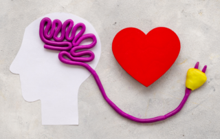 A clay sculpture of a human head with a plug emerging from the brain, symbolizing emotional regulation and mental connection, with a heart placed beside it to represent the link between emotions and cognition.